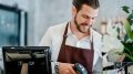 Barista young man scanning QR code or barcode in menu paper at counter in cafeteria.