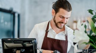 Barista young man scanning QR code or barcode in menu paper at counter in cafeteria.