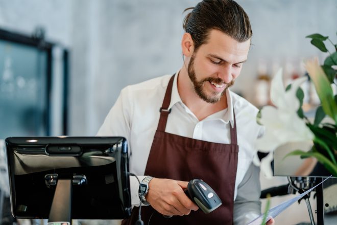Barista young man scanning QR code or barcode in menu paper at counter in cafeteria.