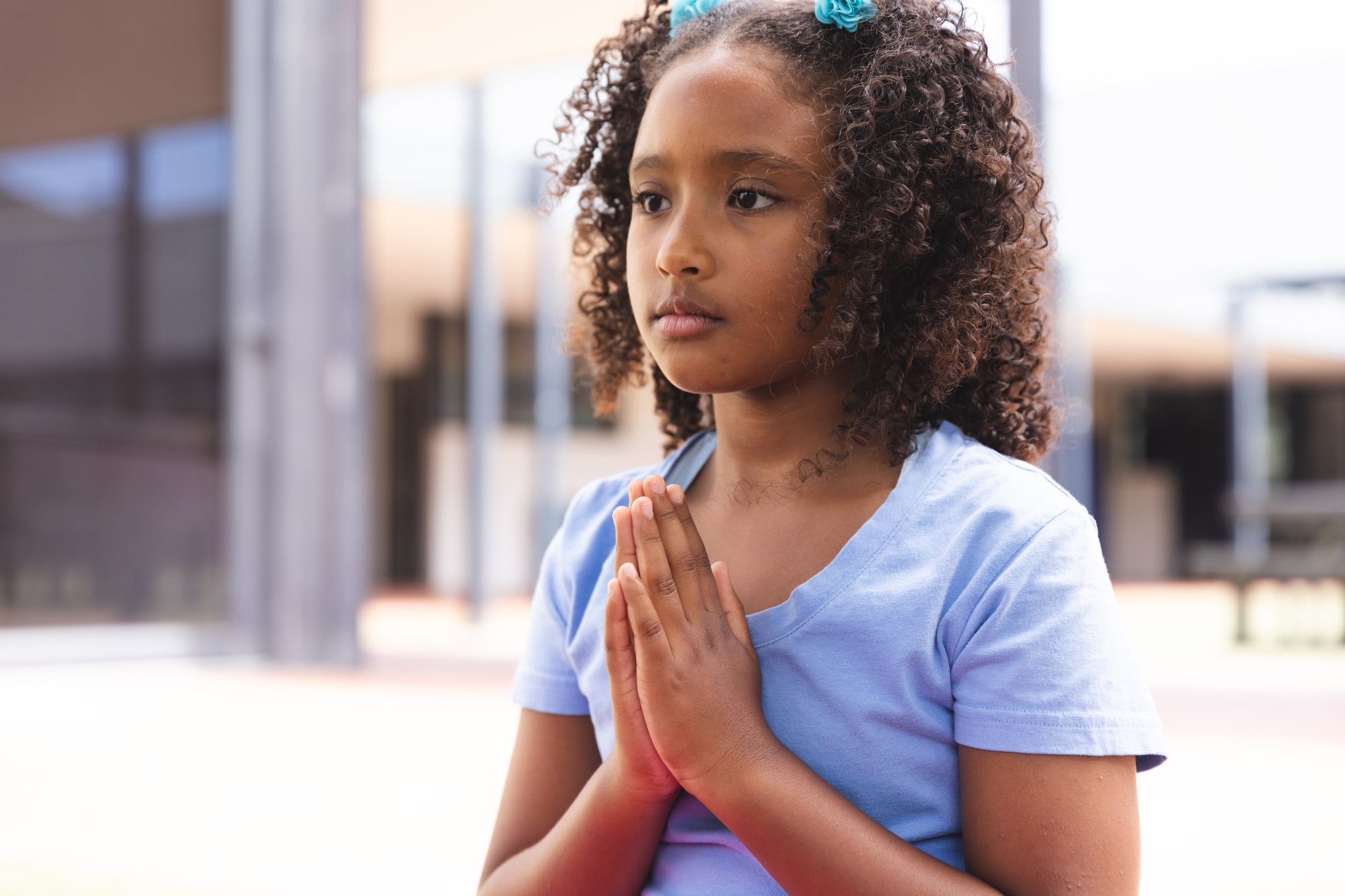 Biracial girl praying outdoors, with copy space