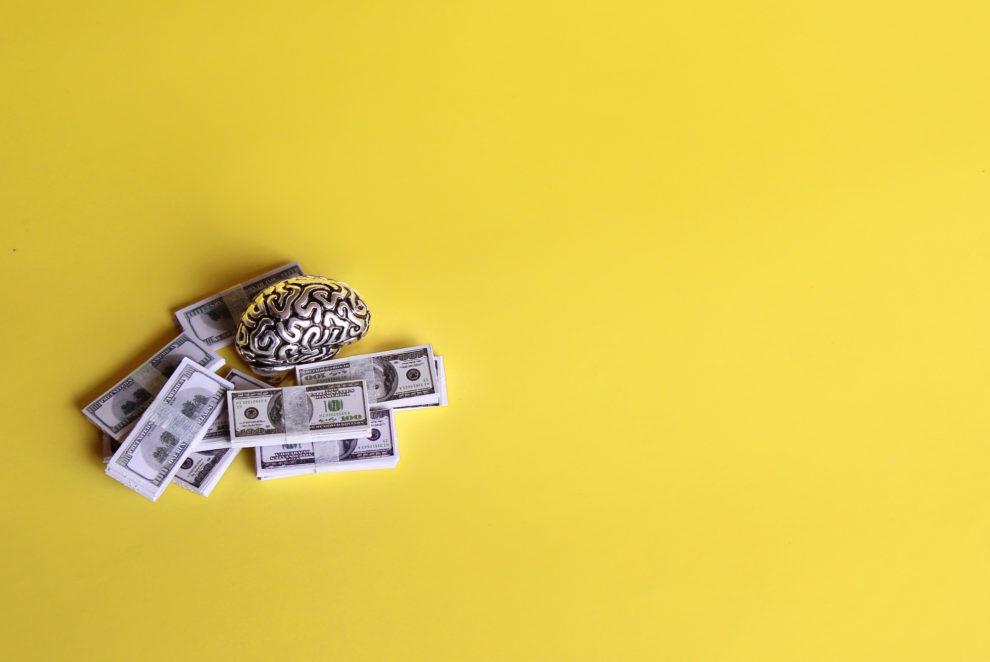 Brain model and stack of money on yellow background.
