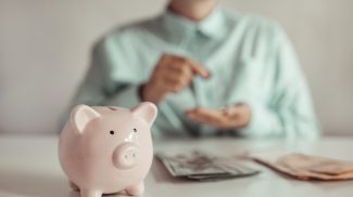Businesswoman considers a bundle of dollar money. Piggy bank on a white table.
