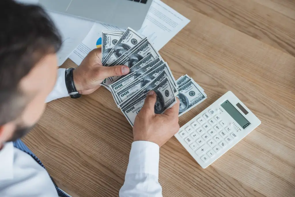 cropped image of financier counting cash with calculator in office
