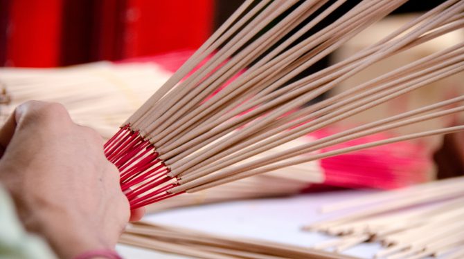 Hands holding and arranging incense sticks with red bases