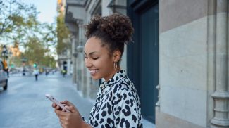 Happy carefree curly haired pretty teenager enjoys positive network messaging in social media holds