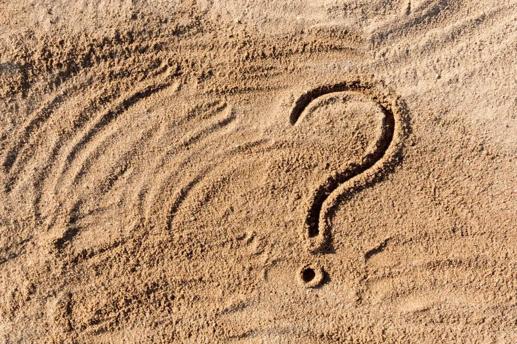 question marks written on beach sand close up, with copy space