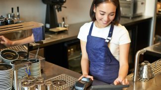 Smiling asian girl barista working in cafe at counter, processing orders, using POS terminal