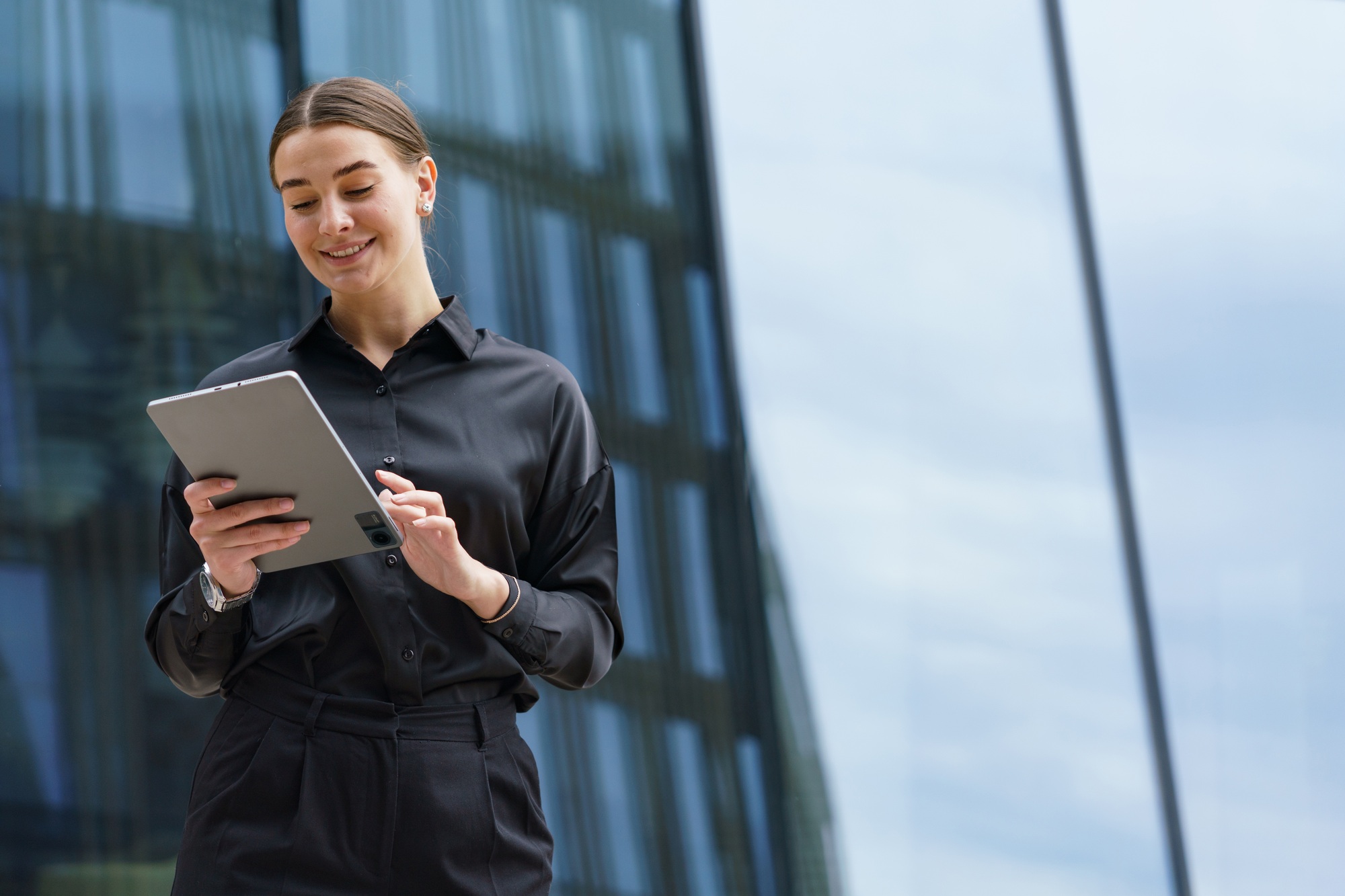 Smiling businesswoman in black, interacting with a tablet, reflects modern professionalism and tech-