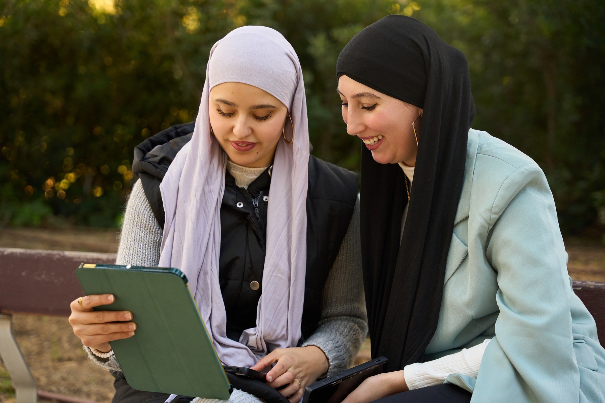 Two muslim businesswomen using tablet and smiling in a park