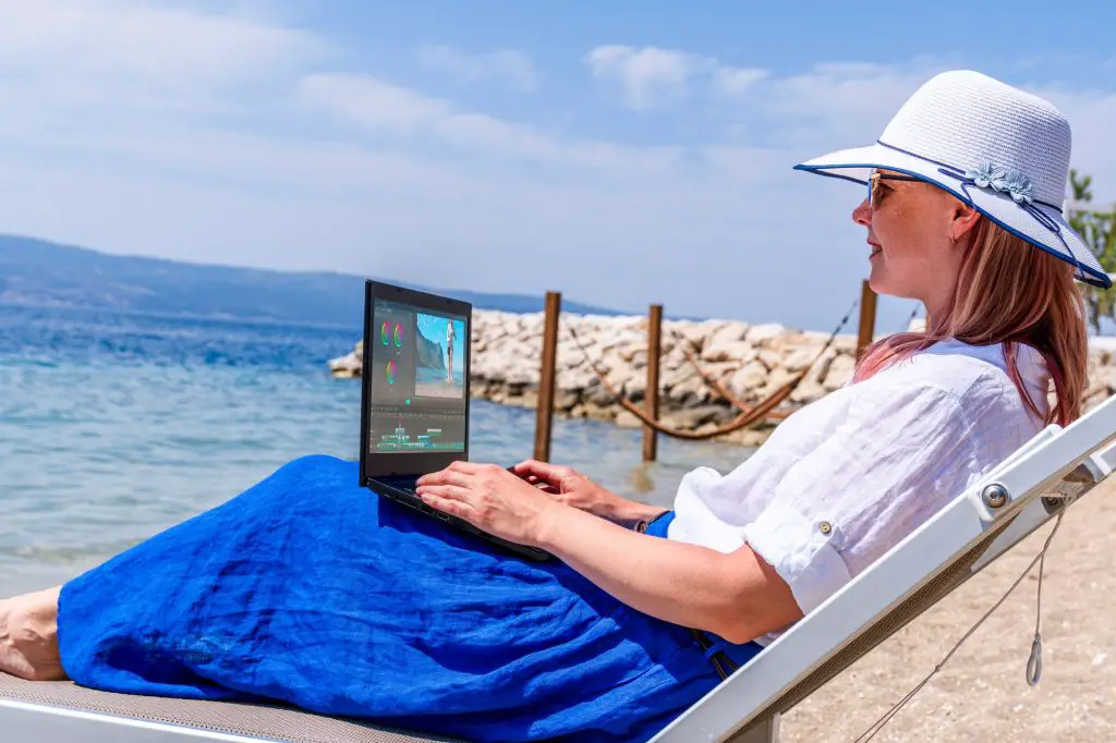 Video blogger, freelancer editing video at beach. Editing Videos On Laptop Using Video Editor App.