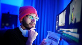 Young man editing video with a focused expression in a dimly lit room at night
