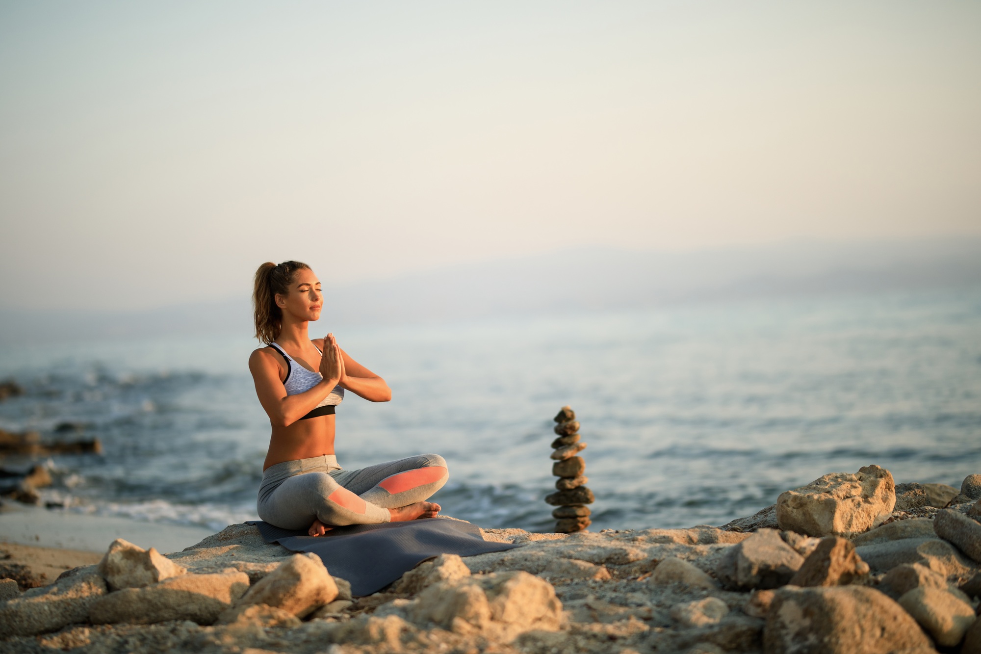 Young woman meditating in prayer position on a beach rock.